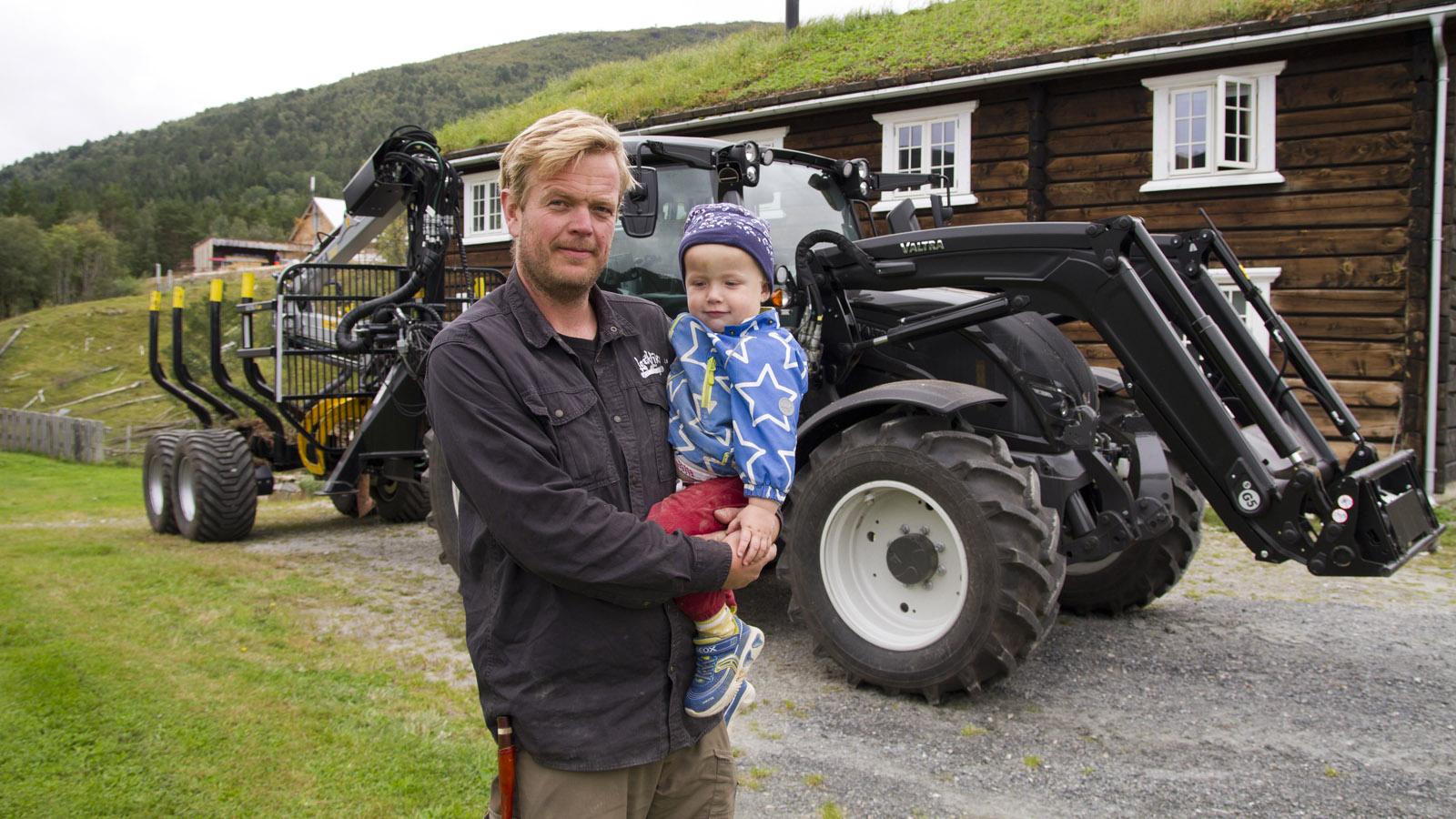 Rolf Trygve Lervik og sønnen Ragnvald på to år foran huset han har laftet til familien på hjemgården. Han bruker Valtra N174 Versu til alt fra frakt av flisvirke og tømmerstokker til å rydde veger i området. 